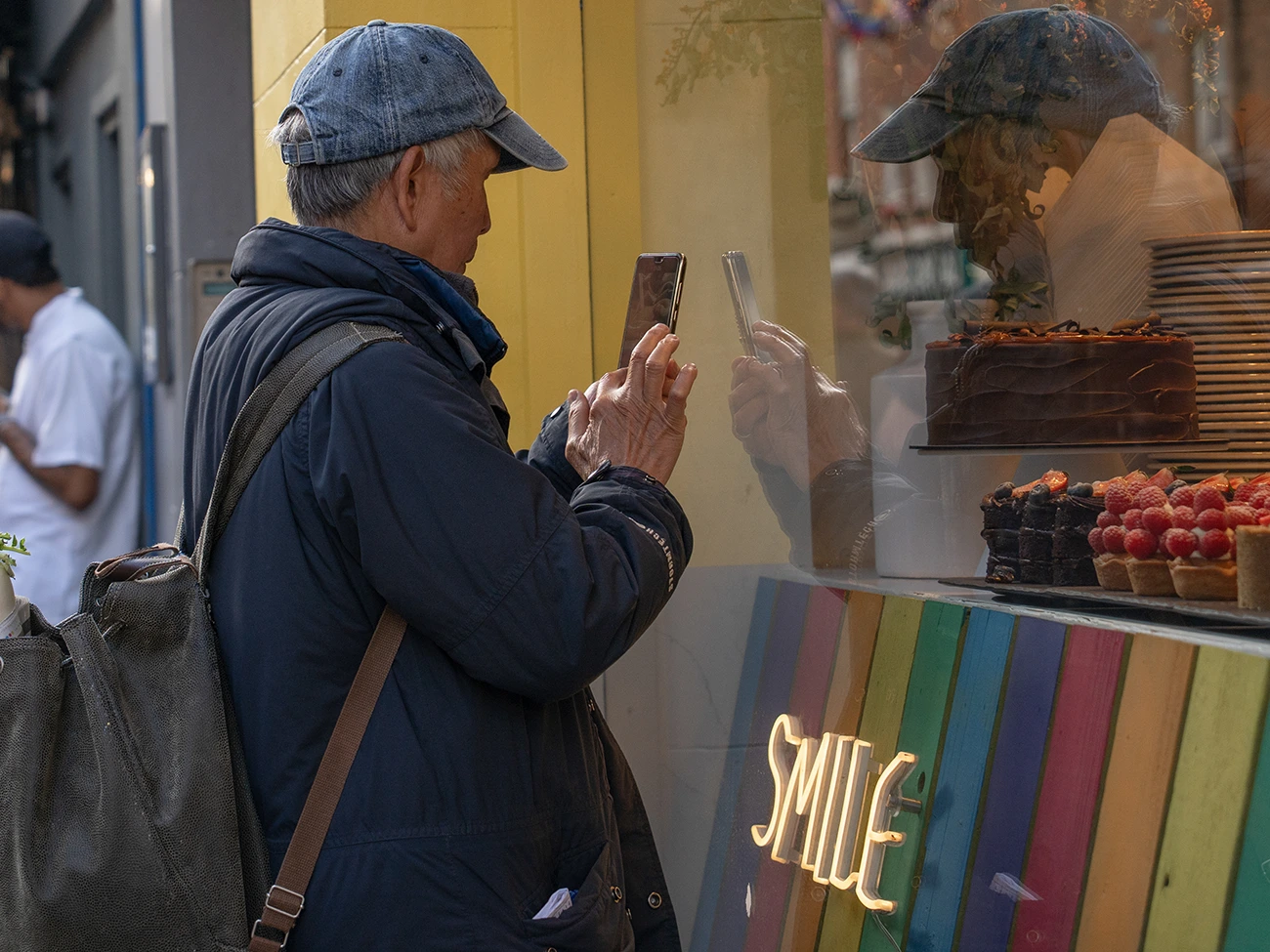 Viajero usando el teléfono frente a una pastelería en Londres con un letrero de neón que dice Smile