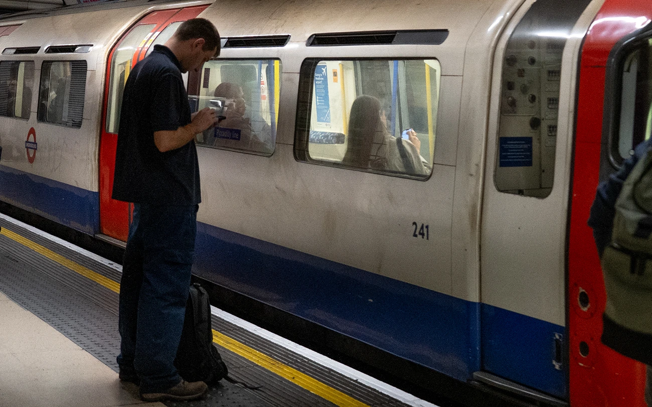 Hombre revisando su teléfono en el andén del metro de Londres junto a un tren