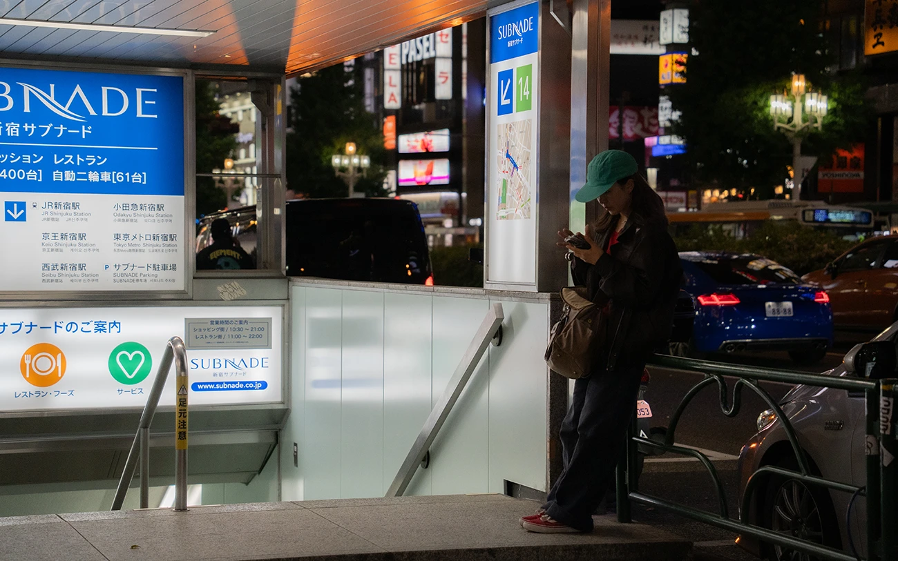 Persona usando el teléfono de noche en una entrada del metro en Shinjuku, Tokio